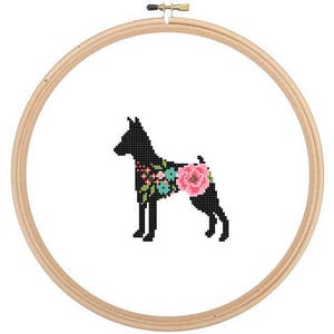 May include: A black silhouette of a dog with floral accents on its back. The dog is standing on a white background and is framed by a wooden hoop.