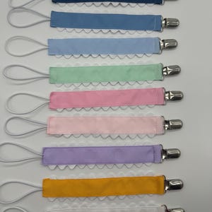 May include: Set of 8 colorful ribbon pacifier clips with white scalloped trim and silver clips. Each clip has a white elastic loop.
