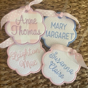 May include: Four pink and white fabric gift tags with blue embroidered names: Anne Thomas, Mary Margaret, Leighton Mae, and Susanna Claire.