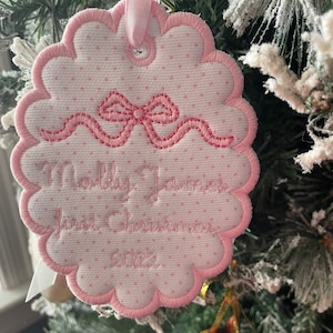 May include: Pink Christmas ornament with a scalloped edge and a pink ribbon bow. The ornament is decorated with white polka dots and the text "Molly James First Christmas 2022".