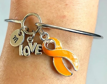 May include: Silver bangle bracelet with a charm that says "LOVE" and an orange ribbon charm. The bracelet also has a small charm with the letter "M" on it.