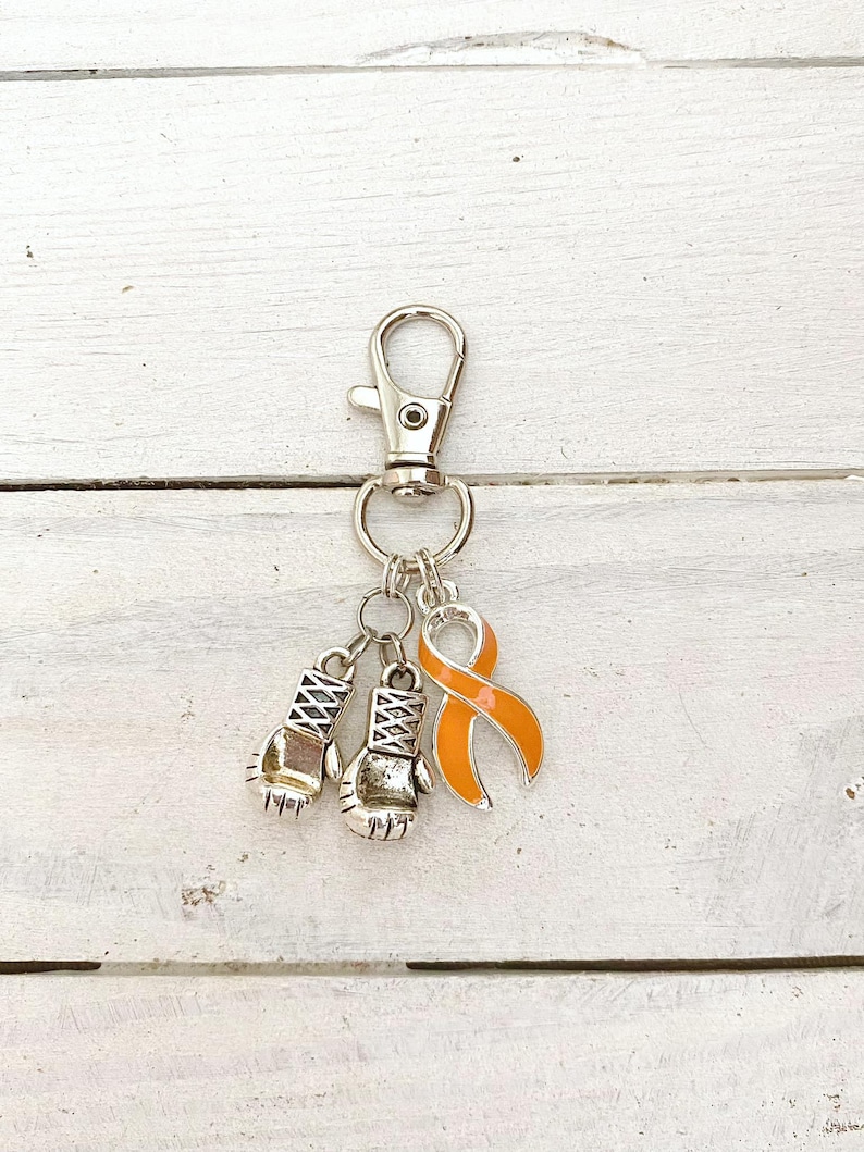 May include: A silver keychain with a silver lobster clasp, two silver boxing glove charms, and an orange ribbon charm.