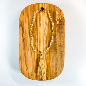 Può includere: Una collana di perline gialle e bianche con un fiocco su una superficie di legno.