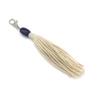May include: A white tassel keychain with a dark blue ceramic bead and a silver metal clasp.