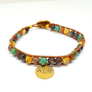 May include: A brown leather wrap bracelet with multi-coloured glass beads and a gold charm with the initials "ALM" engraved on it.