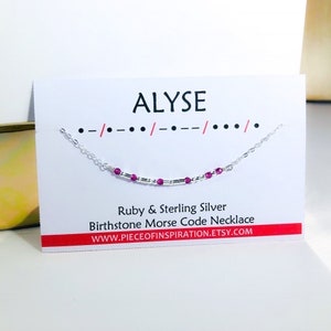 以下が含まれることがあります： 白いカードに黒い文字で「ALYSE」と書かれている。名前の下には、小さな銀色のビーズとピンクのルビーのビーズが付いた銀色のチェーンネックレスがある。「Ruby & Sterling Silver Birthstone Morse Code Necklace」というテキストがネックレスの下に黒文字で書かれている。「WWW.PIECEOFINSPIRATION.ETSY.COM」というテキストがネックレスの下に黒文字で書かれている。