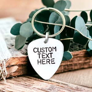May include: Silver guitar pick keychain with a custom text engraving that reads "CUSTOM TEXT HERE".