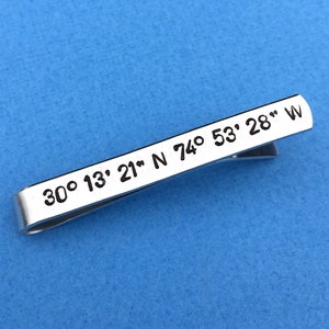 May include: Silver tie clip with the coordinates 30° 13' 21" N 74° 53' 28" W engraved on it.