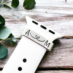 May include: White Apple Watch band with a silver personalized band that says "A ♥ M".
