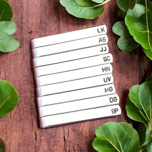 May include: A set of ten silver metal tie clips with engraved initials. The initials are LK, AS, JJ, SC, HN, UV, MG, DG, and BP.