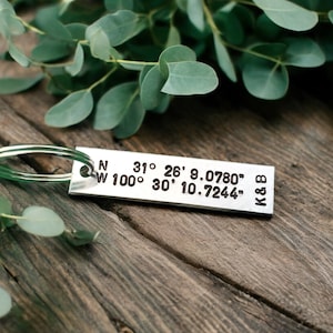 May include: Silver keychain with a metal tag engraved with coordinates: N 31° 26' 9.0780" W 100° 30' 10.7244" and the initials K&B.