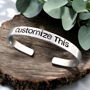May include: Silver metal bracelet with the words "customize this" engraved on it.