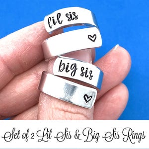 May include: Set of two silver rings with the words "lil sis" and "big sis" engraved on them. Each ring has a small heart engraved on the side.