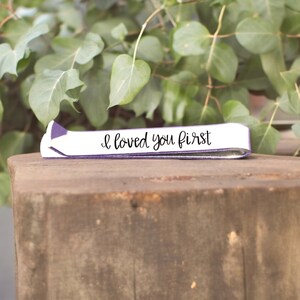 May include: A white leather bracelet with a purple trim and the text "I loved you first" in black script.