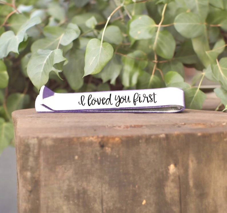 May include: A white leather bracelet with a purple trim and the text "I loved you first" in black script.