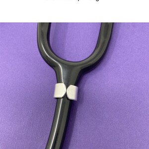 May include: A close-up view of the back of a black stethoscope with a silver tag attached to the tubing.