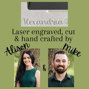 K&ouml;nnte beinhalten: Das Bild zeigt den Namen "Alexandria" lasergraviert auf einer hellen Oberfl&auml;che, mit einem Smiley-Symbol. Der Text lautet "Laser graviert, geschnitten & handgefertigt von Alison & Mike." Der Hintergrund ist ein ged&auml;mpftes Gr&uuml;n.