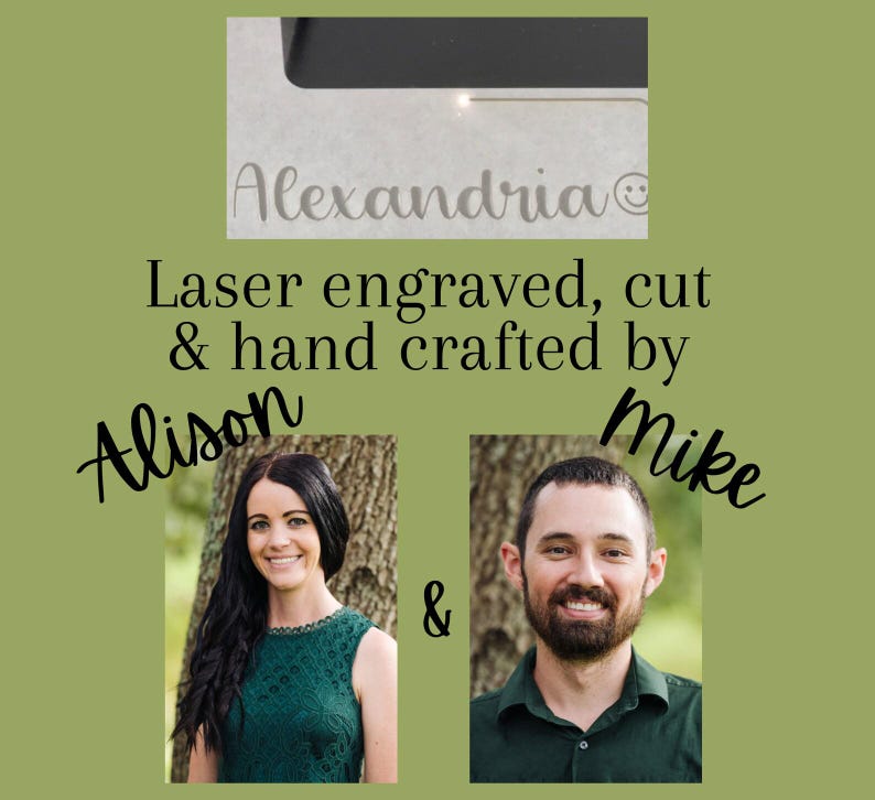 K&ouml;nnte beinhalten: Das Bild zeigt den Namen "Alexandria" lasergraviert auf einer hellen Oberfl&auml;che, mit einem Smiley-Symbol. Der Text lautet "Laser graviert, geschnitten & handgefertigt von Alison & Mike." Der Hintergrund ist ein ged&auml;mpftes Gr&uuml;n.