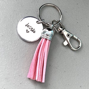 May include: A silver keyring with a pink tassel and a round charm that says "Jessie" with a heart. The keyring has a silver clasp.