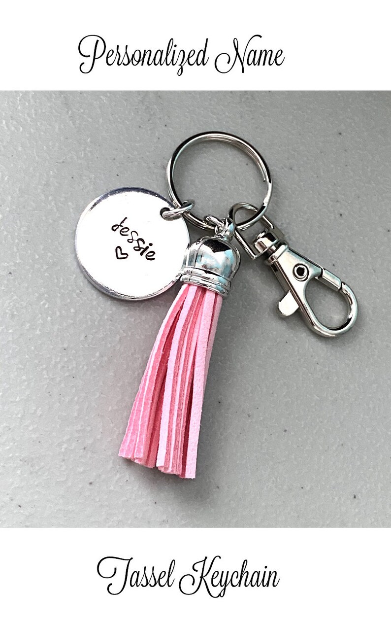 May include: A silver keyring with a pink tassel and a round charm that says "Jessie" with a heart. The keyring has a silver clasp.
