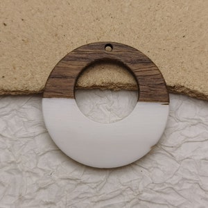 May include: A round wooden and white resin pendant with a hole at the top for hanging. The pendant is half brown wood and half white resin.