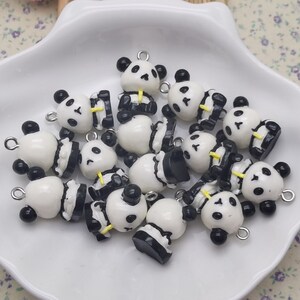 May include: A collection of black and white panda bear charms with black eyes and yellow noses. The charms are made of polymer clay and have a silver loop for attaching to jewelry or other crafts.