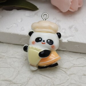 May include: A white and black panda bear charm with a yellow and orange outfit and a white chef's hat. The charm has a silver loop for attaching to a necklace or bracelet.