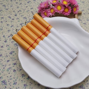 May include: Six white and orange cigarette-shaped charms with silver rings on top, displayed on a white plate.