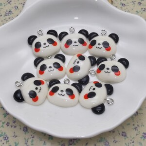 May include: A collection of eight white panda face charms with black eyes and red cheeks. Each charm has a silver loop for attaching to jewelry or other crafts.