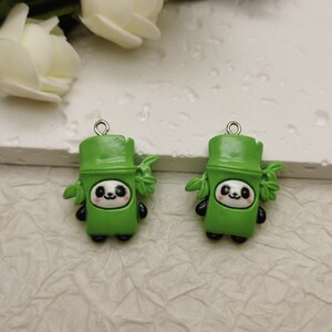 May include: Two green panda bear charms. Each charm features a panda face with black and white details, set within a green bamboo-shaped body. Small silver loops are attached at the top for hanging.