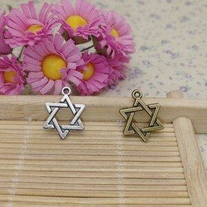 May include: Two silver and gold Star of David charms on a wooden background. The charms are both in the shape of a six-pointed star.