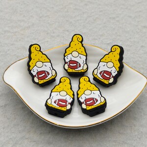 May include: Five gnome-shaped charms with yellow hats and black outlines, each holding a football. The gnomes are arranged on a white, gold-rimmed dish. The footballs are red and white.