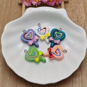May include: Six colorful heart-shaped lollipop charms with a swirl design and a bow. The charms are made of resin and have a silver-toned metal loop for attaching to jewelry or crafts.