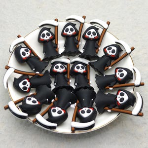 May include: A collection of miniature Grim Reaper figurines, each with a black robe, white skull face, and a scythe. The figurines are arranged on a white plate with a gold rim, set against a neutral background.