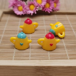 Puede incluir: Cuatro teteras amarillas en miniatura con detalles azules y rojos. Las teteras están sobre una superficie de madera.