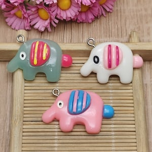 May include: Three colourful elephant charms with silver jump rings. The elephants are made of polymer clay and have different coloured stripes on their backs. The elephants are green, white, and pink.