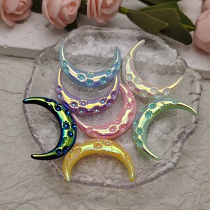 Puede incluir: Un conjunto de seis dijes de media luna iridiscentes con un diseño floral. Los dijes están hechos de plástico y tienen una variedad de colores, incluyendo azul, morado, rosa y amarillo.