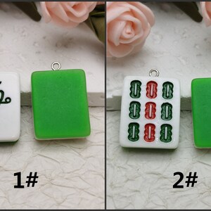 Puede incluir: Dos fichas de mahjong de cer&aacute;mica blanca con lazos de metal plateado. La primera ficha tiene un dise&ntilde;o de p&aacute;jaro verde con un ojo rojo. La segunda ficha tiene un patr&oacute;n rojo y verde. Ambas fichas tienen un fondo verde.