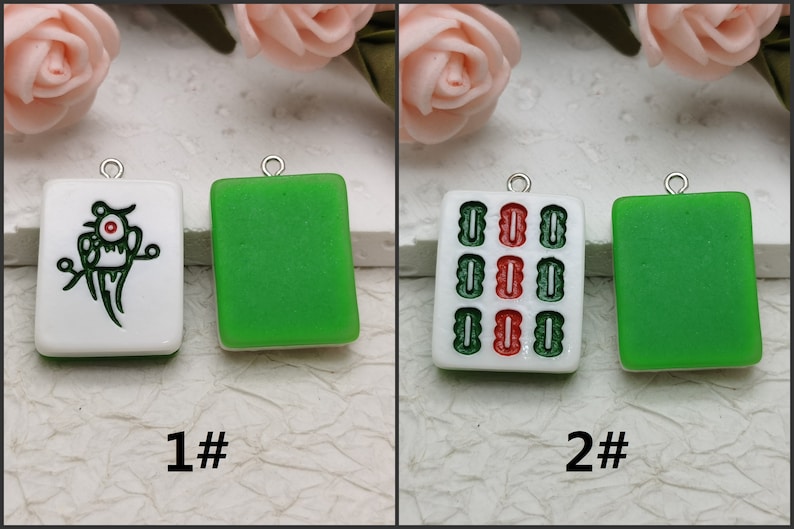 Puede incluir: Dos fichas de mahjong de cer&aacute;mica blanca con lazos de metal plateado. La primera ficha tiene un dise&ntilde;o de p&aacute;jaro verde con un ojo rojo. La segunda ficha tiene un patr&oacute;n rojo y verde. Ambas fichas tienen un fondo verde.
