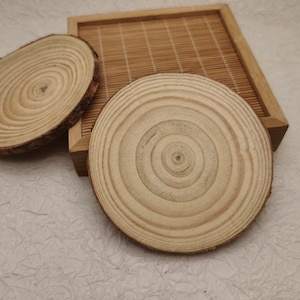 May include: Three round wooden coasters with a natural wood finish. The coasters have a concentric circle pattern.