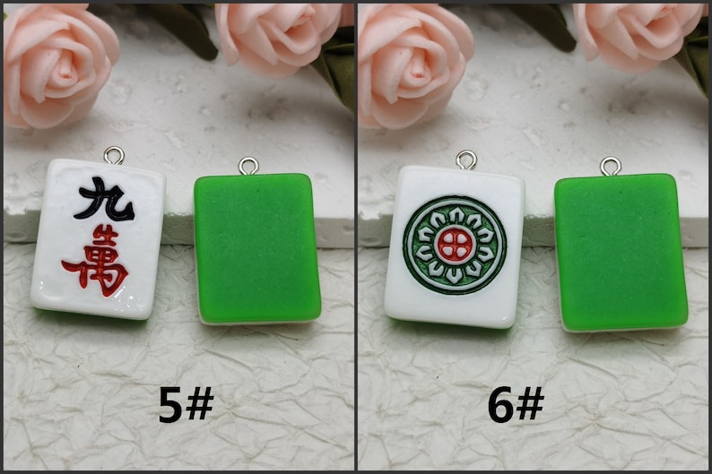 Puede incluir: Dos fichas de mahjong de cer&aacute;mica blanca con caracteres negros y rojos y un dise&ntilde;o de c&iacute;rculo verde. Una ficha tiene los caracteres chinos para "Nueve bamb&uacute;" y la otra tiene un c&iacute;rculo verde con una cruz roja en el centro. Ambas fichas tienen un lazo plateado para colgar.
