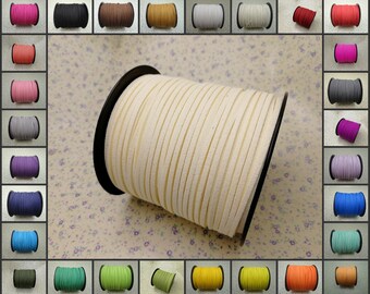 May include: A spool of off-white suede cord, approximately 3mm wide, is shown on a floral patterned background. The cord is wound around a black plastic spool. A variety of colors of the same cord are shown in smaller spools around the main image.