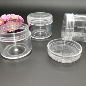 Puede incluir: Cuatro tarros de plástico transparente con tapas. Los tarros son cilíndricos y tienen un acabado liso y brillante. Las tapas también son de plástico transparente y tienen un acabado ligeramente texturizado.