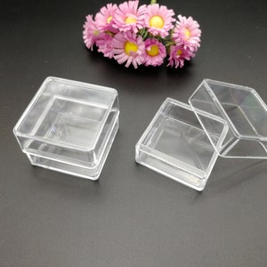 Puede incluir: Tres cajas de plástico transparente, dos apiladas una encima de la otra y una abierta. Las cajas son cuadradas y tienen un acabado liso y brillante.