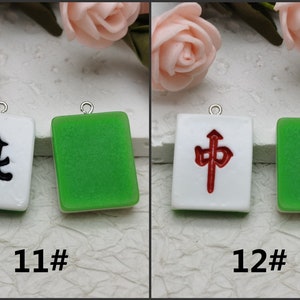 Puede incluir: Dos fichas de mahjong de cer&aacute;mica blanca con caracteres chinos negros y rojos. La ficha de la izquierda tiene un car&aacute;cter negro y la ficha de la derecha tiene un car&aacute;cter rojo. Ambas fichas tienen un borde verde.
