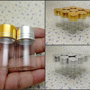 Może przedstawiać: Zestaw przezroczystych szklanych butelek z srebrnymi i złotymi pokrywkami. Butelki są małe i cylindryczne. Idealnie nadają się do przechowywania olejków eterycznych, perfum lub innych płynów.