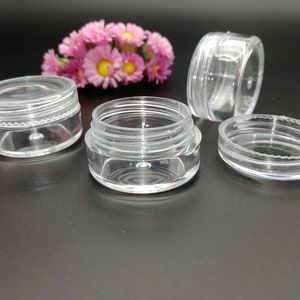 Op de afbeelding: Vier transparante plastic containers met deksels. De containers zijn rond en hebben een gladde, glanzende afwerking. Ze zijn perfect voor het opbergen van kleine items zoals sieraden, cosmetica of knutselspullen.