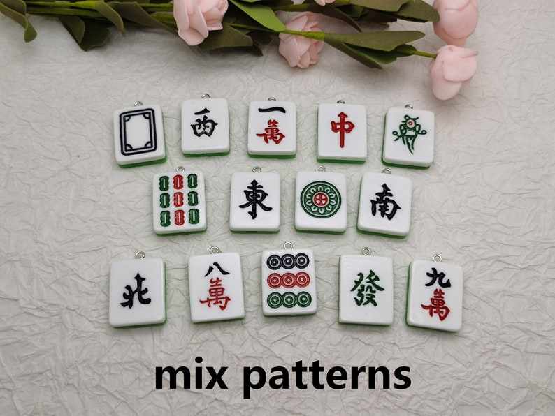 Puede incluir: Una colecci&oacute;n de 12 fichas de mahjong chinas blancas y verdes con varios s&iacute;mbolos y caracteres. Las fichas est&aacute;n dispuestas en tres filas de cuatro. Las fichas son todas diferentes, pero todas tienen un dise&ntilde;o similar. Las fichas miden aproximadamente 5 cm de largo y 2,5 cm de ancho.