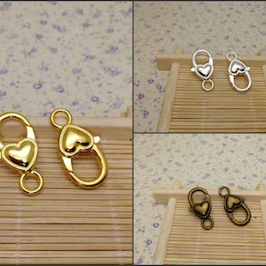 Könnte beinhalten: Zwei goldene herzförmige Verschlüsse mit einer federbelasteten Öffnung. Die Verschlüsse befinden sich auf einer Holzoberfläche.