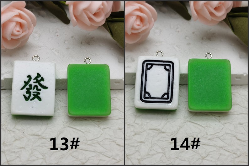 Puede incluir: Dos fichas de mahjong chinas verdes y blancas con dijes plateados. La primera ficha tiene un fondo blanco con caracteres chinos negros. La segunda ficha tiene un fondo blanco con un borde negro y un dise&ntilde;o negro en el interior.